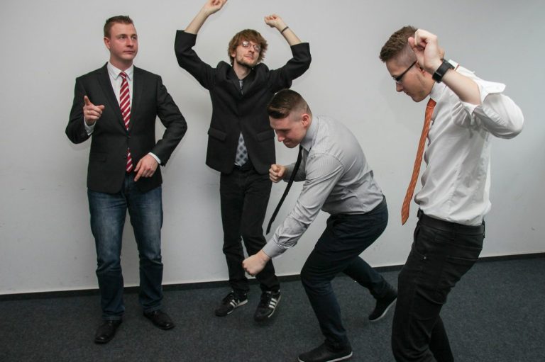 Erhöhtes Wohlbefinden Vier Männer in Anzügen feiern ausgelassen in einem modernen Raum ihre Mitarbeiterzufriedenheit.